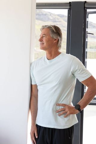 Mature man leaning and gazing through window at hillside view in minimalist studio