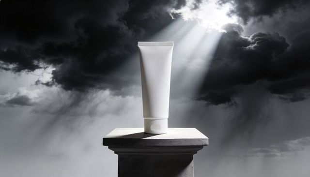 Showcasing white cosmetic tube on stone pedestal under dramatic sunbeam for minimalist beauty