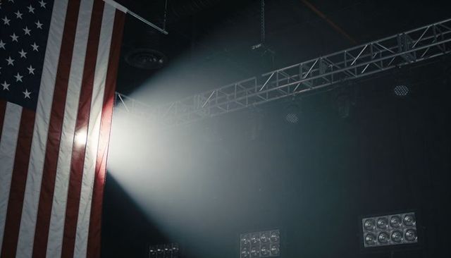 American Flag Catching Spotlight on Foggy Stage with Truss, Rigging and Dramatic Beam