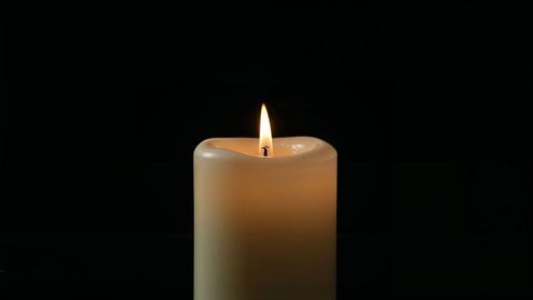 Ivory pillar candle against black background illuminating dark studio for condolences