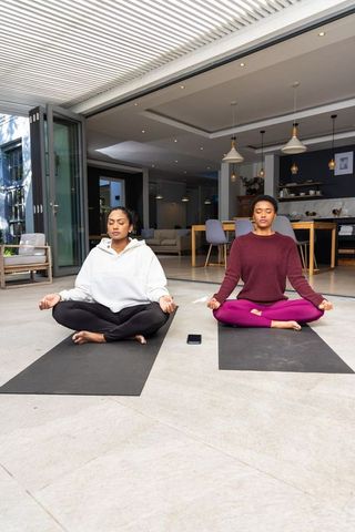 Diverse women meditating on patio mats at modern home threshold practicing mindfulness