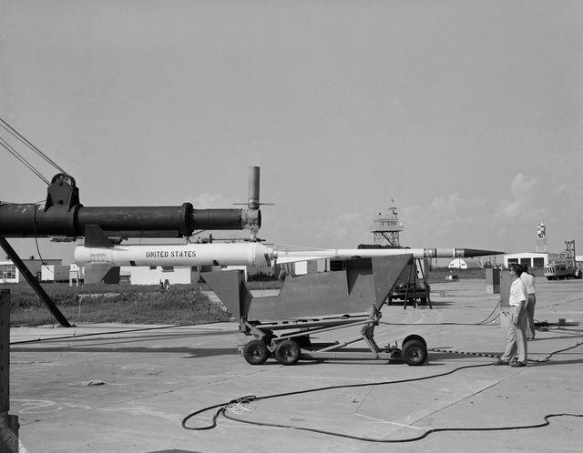 Image depicts Nike Asp missile being prepared at a launching facility in USA. Ideal for use in historical articles about military technology, Cold War era missile advancements, and educational purposes to show military preparations. Black and white format conveys historical context.