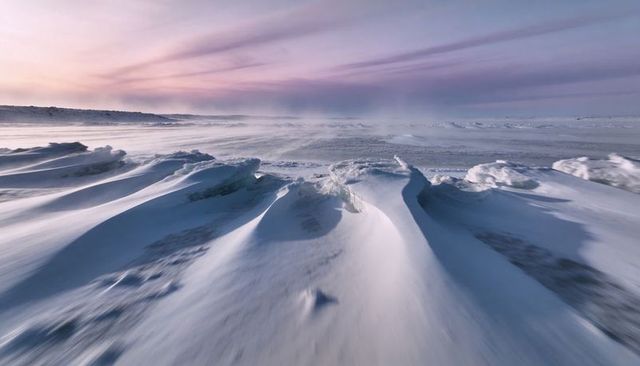 Wind-sculpting snowdrifts and breaking shore ice on frozen coastline at pastel dawn