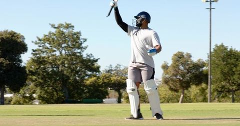 Black cricketer raising bat while preparing to face ball on green pitch
