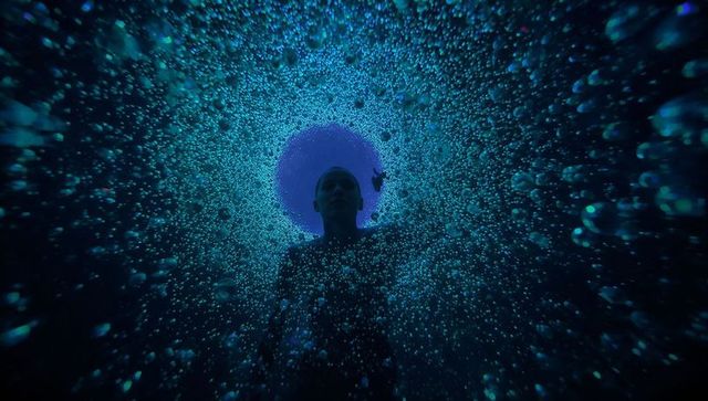 Floating silhouette drifting toward glowing pool surface through turquoise bubble tunnel