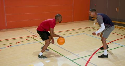 African american men playing one-on-one basketball, dribbling and defending on indoor court