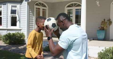 Father and son balancing soccer ball on foreheads in sunny suburban front yard
