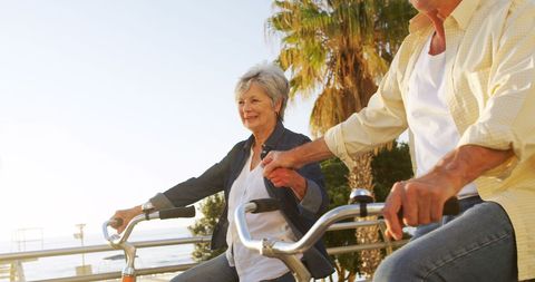 Senior Couple Biking by Sea Holding Hands Promoting Togetherness - Download Free Stock Images Pikwizard.com