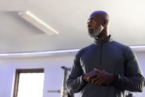 Confident senior man training in gym wearing performance zip-top and fitness tracker