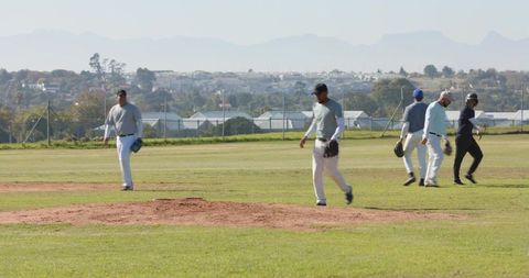 Diverse male baseball teammates walking across sunlit grass field near pitcher mound