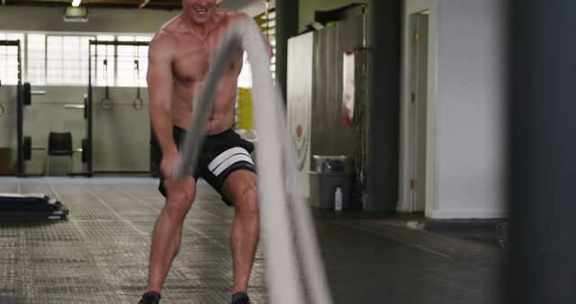 A middle-aged Caucasian man is vigorously exercising with battle ropes in a gym, with copy space. His intense workout showcases a focus on strength and cardiovascular fitness.