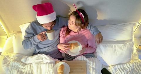 Couple enjoying cozy christmas breakfast in bed wearing santa hat and candy cane headband