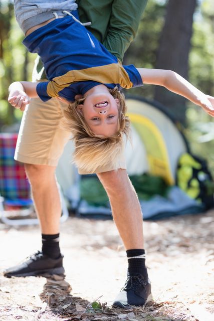 Playful father holding son upside down at campsite