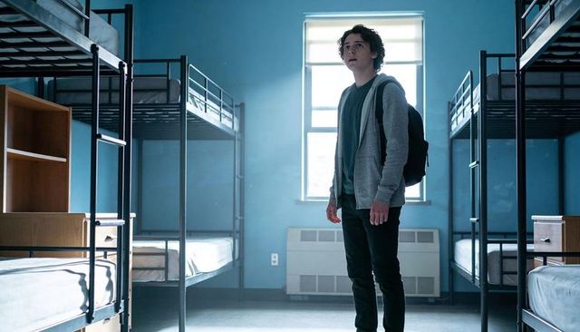 Teen standing in empty dorm room bathed in window light contemplating new chapter