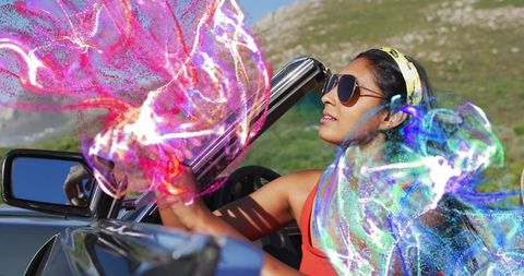 Woman driving convertible along coastal hills with vibrant abstract color trails and shades