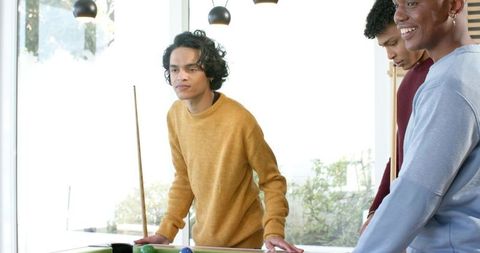 Young men playing pool in sunlit game room showing casual camaraderie at billiards table