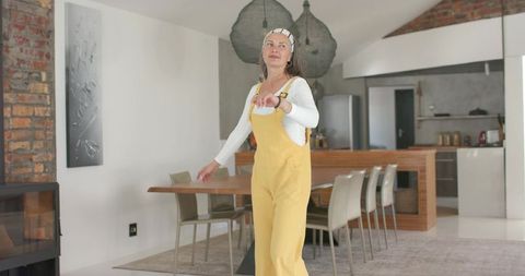 Mature woman wearing mustard overalls checking wristwatch in modern open-plan kitchen