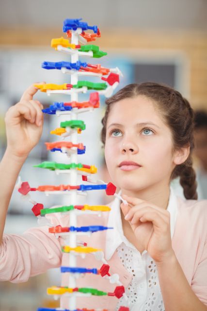 Young schoolgirl building a colorful molecular model in a science class laboratory. Ideal for educational content, STEM promotion, school projects, and science-related articles. Perfect for illustrating hands-on learning and student engagement in academic settings.