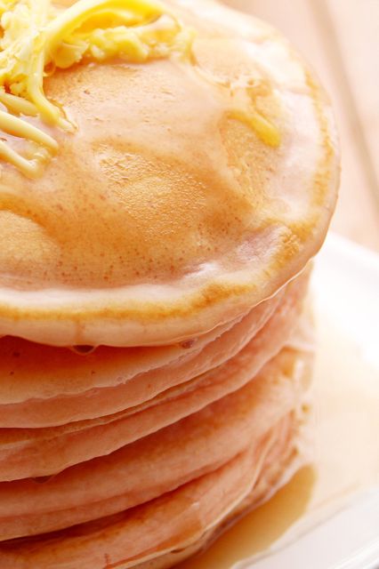 Ideal for food blogs, restaurant menus, and breakfast-themed promotions, this image showcases a close-up view of a stack of fluffy pancakes topped with melted butter and drizzled with syrup.