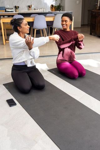 Diverse women stretching and smiling on yoga mats during home partner fitness session