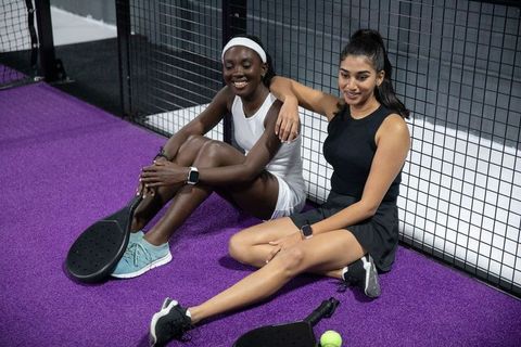 Diverse female teammates relaxing on purple paddle court after friendly match