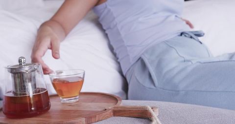 Morning tea ritual in bed woman reaching for teacup on wooden tray cozy loungewear