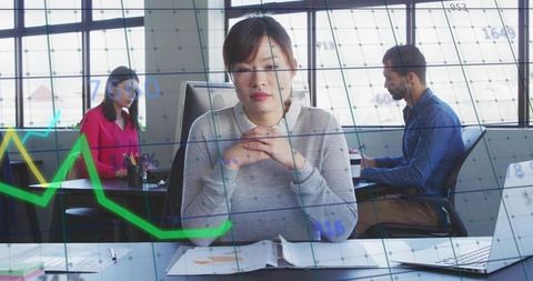 Woman reviewing binder with overlaying financial charts in modern open office workspace