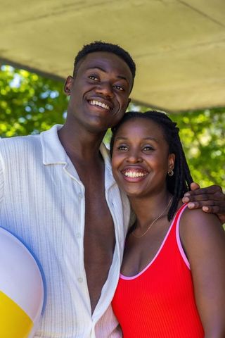 African american couple smiling and holding beach ball in sunny park wearing red swimwear