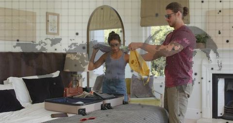 Young couple packing for international trip in stylish bedroom with world map graphic