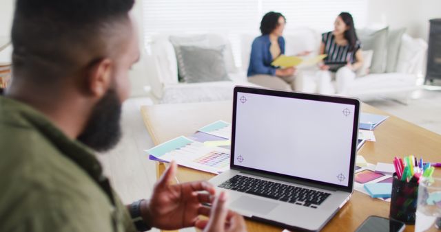 African american man making laptop image call, copy space on screen, colleagues behind, slow motion. Working from home, small business, friendship and start up business concept.