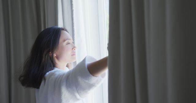 Happy asian woman drawing bedroom curtains on sunny morning. Lifestyle, morning, free time, wellbeing and domestic life, unaltered.