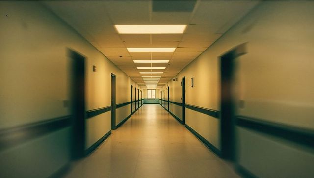 Empty hospital corridor with fluorescent lighting and distant window