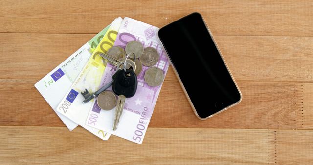 Euro banknotes and coins are placed next to a smartphone and car keys on a wooden surface, with copy space. This setup suggests a concept of financial transactions, personal budgeting, or the cost of automotive ownership and technology.