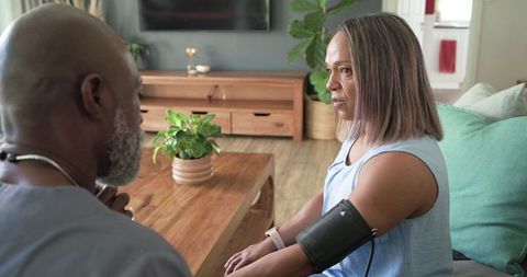 African american caregiver measuring blood pressure for female patient during home visit