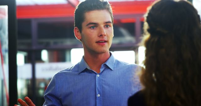 Man explaining something to a woman in an office light environment. The man wears a blue shirt, and their setting appears professional. The scene suggests a business meeting, teamwork, or work-related discussion. Useful for illustrating office communication, collaboration, or professional interactions.