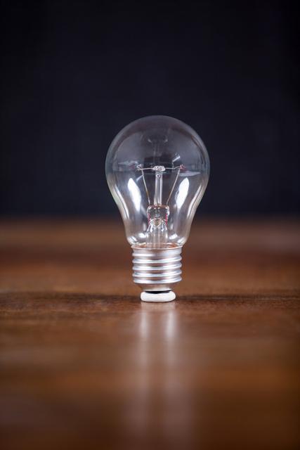 This image features a close-up view of an electric bulb placed on a wooden floor. The clear glass and visible filament emphasize the simplicity and functionality of the bulb. Ideal for use in articles or advertisements related to electricity, innovation, energy efficiency, and minimalist design.