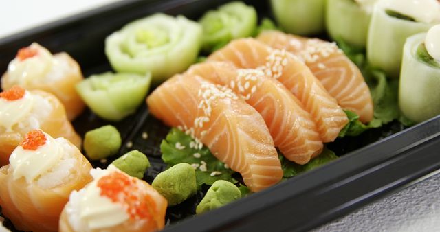 Close-up view of assorted fresh sushi featuring salmon sashimi slices garnished with sesame seeds, along with wasabi and cucumber. Ideal for use in promotions for Japanese restaurants, culinary blogs, and healthy eating infographics.