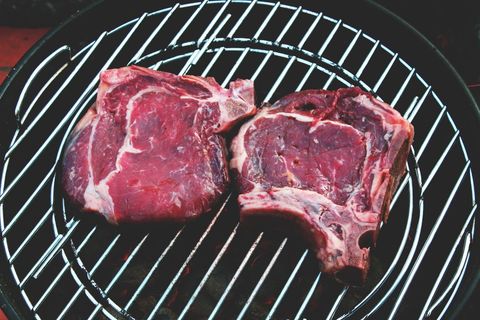 Raw Bone-In Ribeye Steaks on Charcoal Grill Preparing for Backyard Barbecue