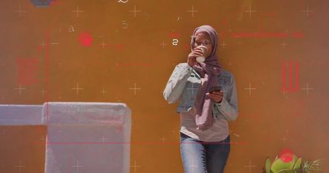 Stylish woman in hijab enjoying coffee and smartphone