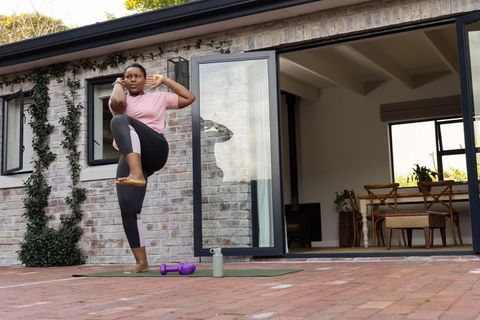 African american woman practicing balance kick on patio during outdoor home workout