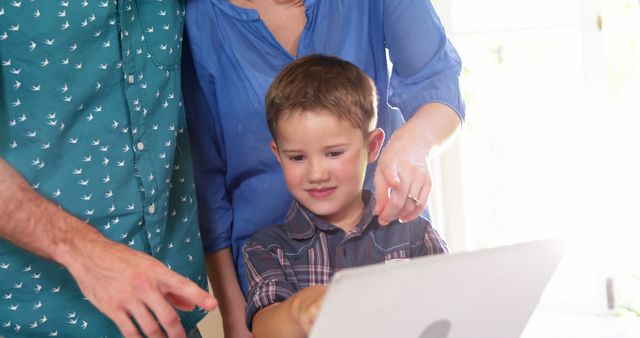 A young boy being guided by his parents while using a laptop at home. Ideal for illustrating themes of family bonding, education, technology use in homes, and parental guidance.