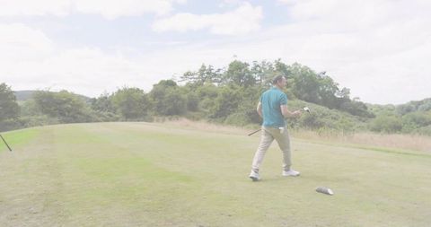 Golfer walking across tee box in teal polo on countryside fairway with copy space