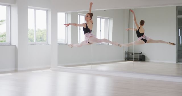 Young ballerina practicing grand jeté in a well-lit dance studio. Reflective mirrors and large windows enhance the spacious and clean environment. Suitable for themes related to ballet training, performing arts, discipline, grace, and athleticism.