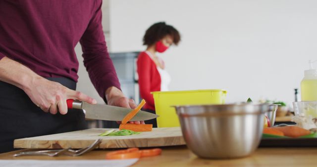 Focused Chef Slicing Carrots in Modern Kitchen while Assistant Stands in Background - Download Free Stock Images Pikwizard.com