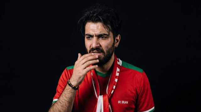 Tense iranian football fan holding hand to mouth wearing red jersey and scarf