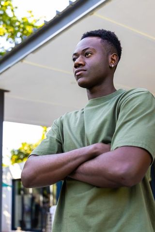 Confident young man standing with arms crossed wearing olive-green t-shirt and hoop earring