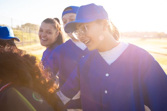 Diverse group of young female baseball players in blue uniforms motivating each other before a game. Ideal for use in sports-related content, team-building articles, and promotional materials for women's sports. Highlights themes of teamwork, motivation, and athleticism.