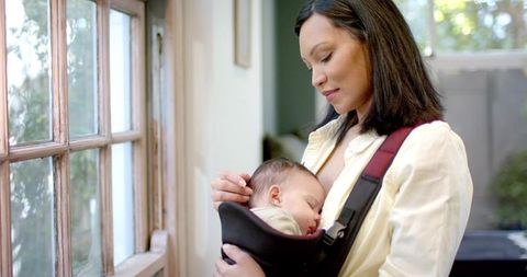 Mother bonding with sleeping baby by bright window in peaceful living room