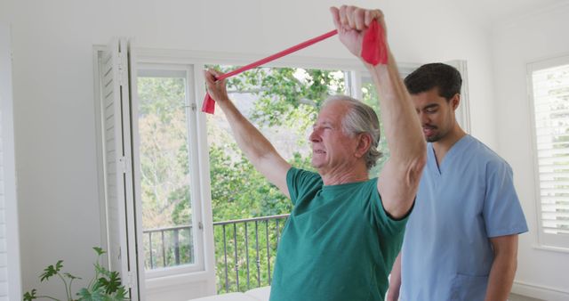 Senior man undergoing physiotherapy session using a resistance band, assisted by a professional physiotherapist. This might be used for healthcare, elder care, rehabilitation, geriatric fitness programs, or healthy aging promotions.