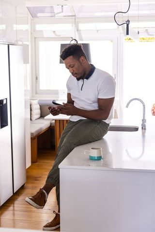 Man sitting on kitchen island reviewing documents and checking phone in sunlit modern kitchen
